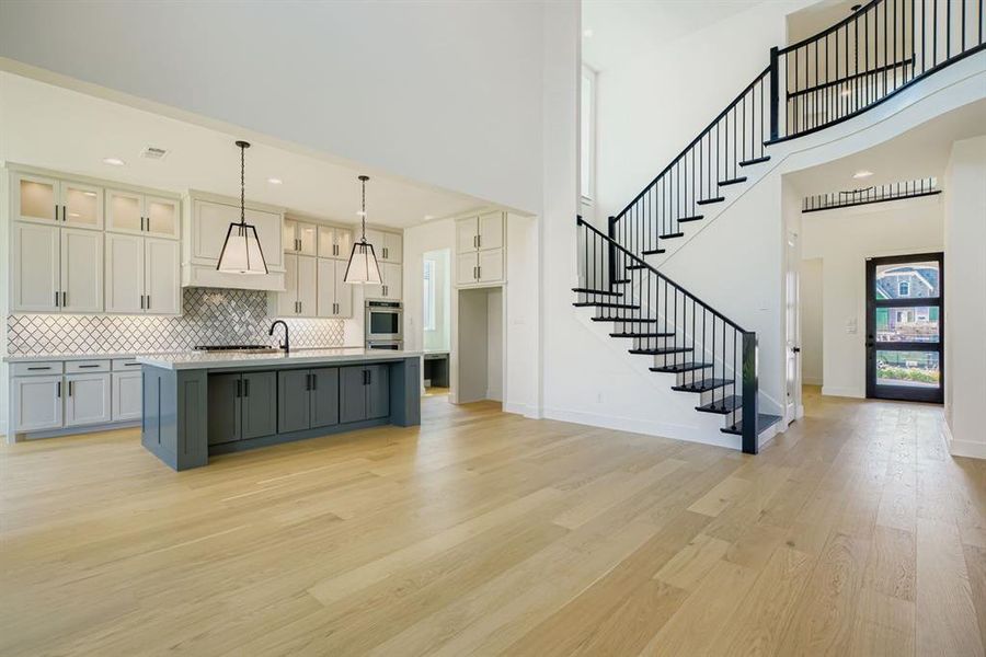 Kitchen featuring tasteful backsplash, light wood-type flooring, an island with sink, white cabinets, and hanging light fixtures Kitchen featuring tasteful backsplash, light wood-type flooring, an island with sink, white cabinets, and hanging light fixtures