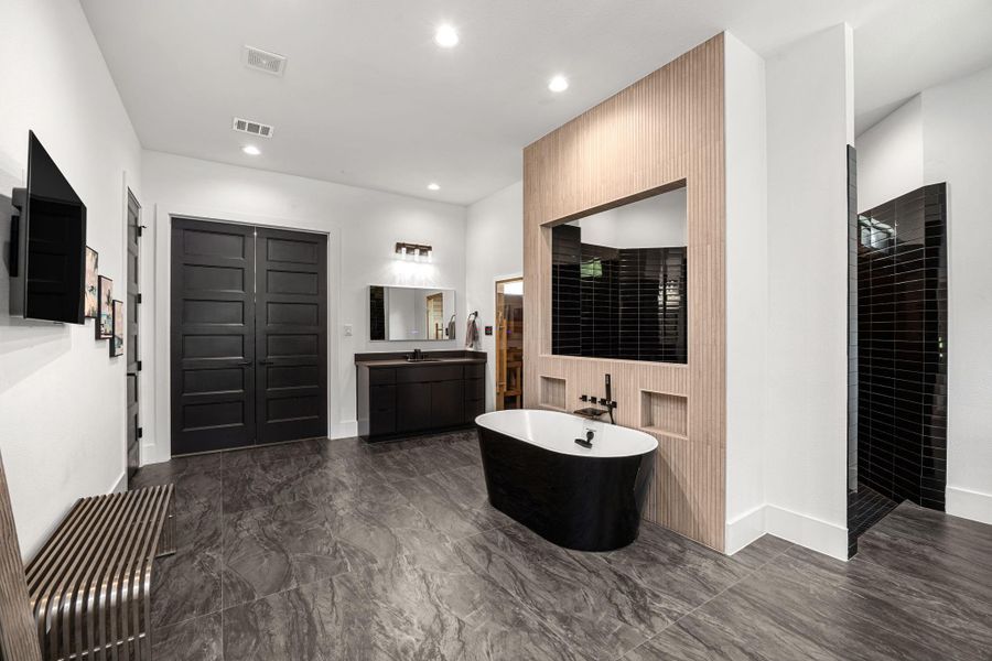 This spacious bathroom features a modern design with a sleek black freestanding tub, black tile accents, and a large double vanity. It has a contemporary aesthetic with dark doors and floors, accented by bright lighting. This spacious bathroom features a modern design with a sleek black freestanding tub, black tile accents, and a large double vanity. It has a contemporary aesthetic with dark doors and floors, accented by bright lighting.