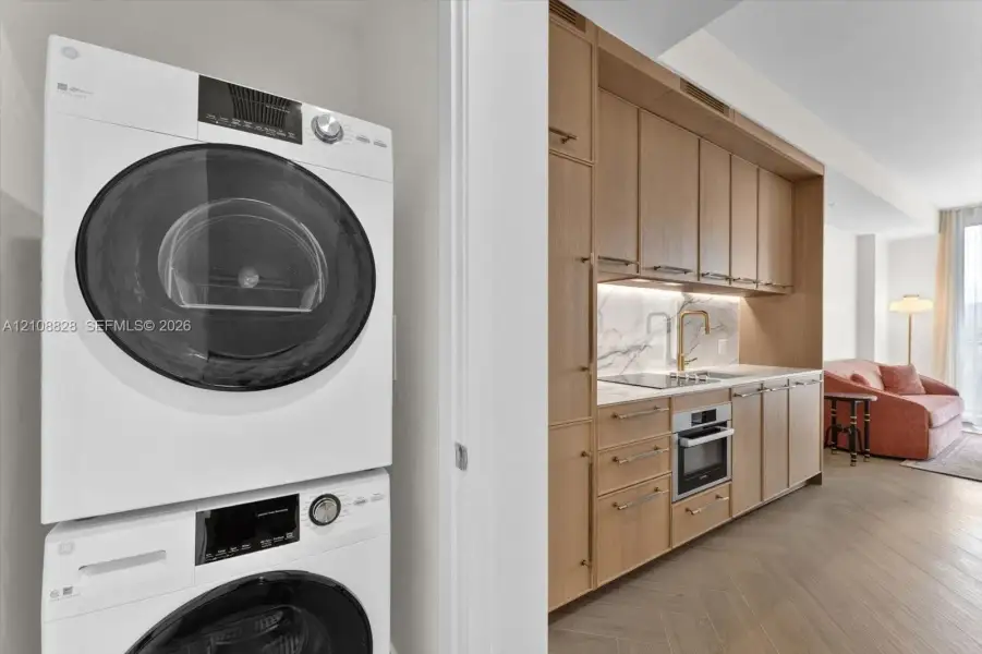 Stacked laundry unit with wood-finish cabinetry, stone-surface backsplash, integrated cooktop, and herringbone wood-finish flooring