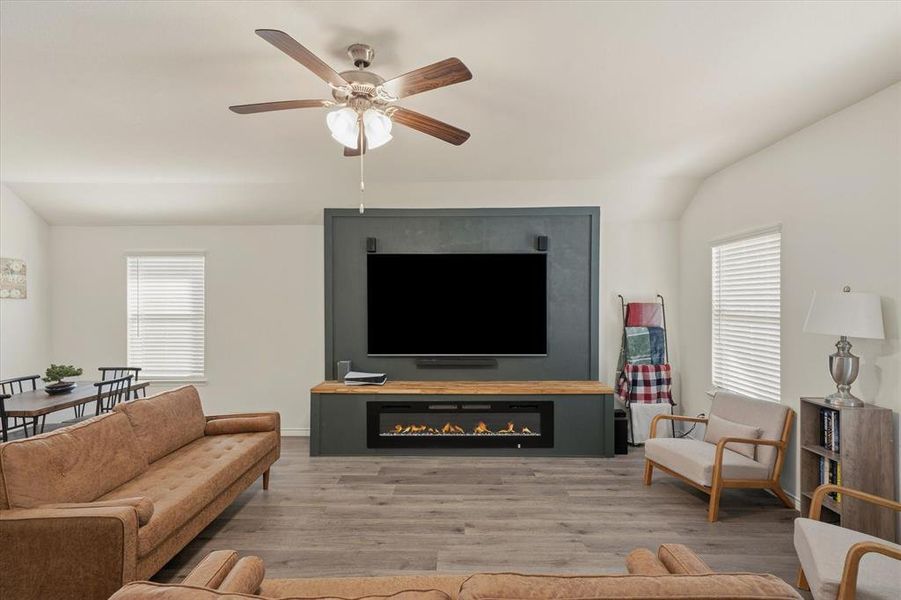 Living area featuring wood finished floors, a ceiling fan, a glass covered fireplace, and lofted ceiling Living area featuring wood finished floors, a ceiling fan, a glass covered fireplace, and lofted ceiling