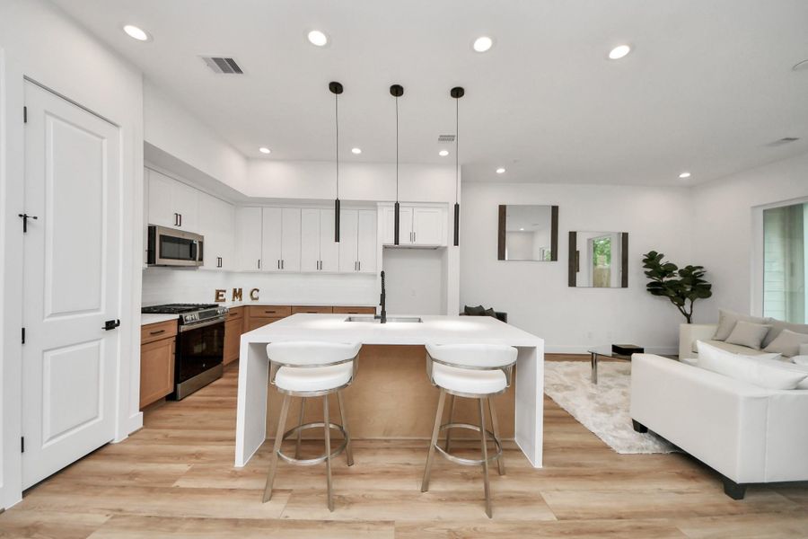 This kitchen boasts a sleek, modern design with elegant pendant lighting, a spacious island perfect for gathering, and seamless integration into the open-concept living area, creating an inviting and stylish heart for your home.