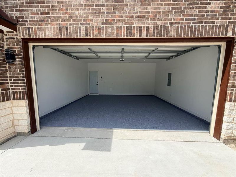 Spacious two-car garage featuring an epoxy-coated concrete floor, white painted walls, and a side access door Spacious two-car garage featuring an epoxy-coated concrete floor, white painted walls, and a side access door