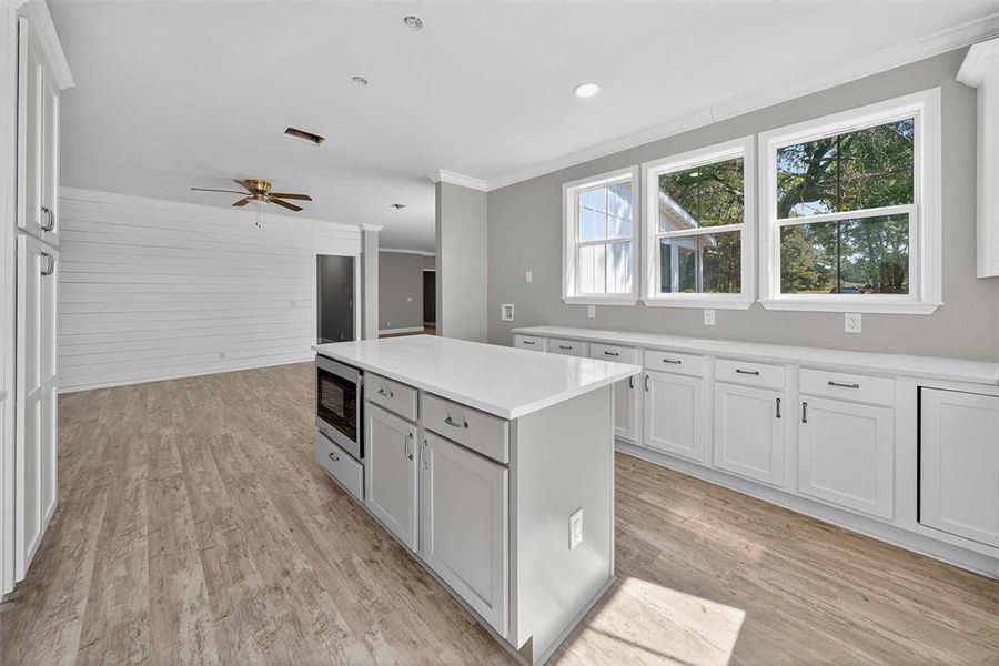 Kitchen featuring crown molding, white cabinets, a center island, light wood finished floors, and ceiling fan