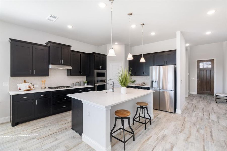 Kitchen featuring light hardwood / wood-style floors, hanging light fixtures, a kitchen breakfast bar, a center island with sink, and appliances with stainless steel finishes