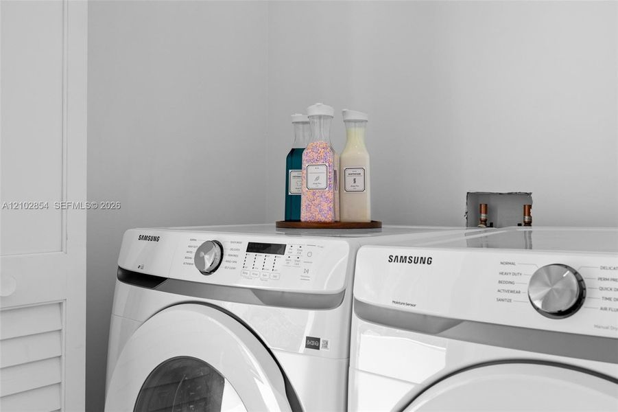Laundry space featuring white front-load washer and dryer units with digital control panels and metallic finish dial selectors