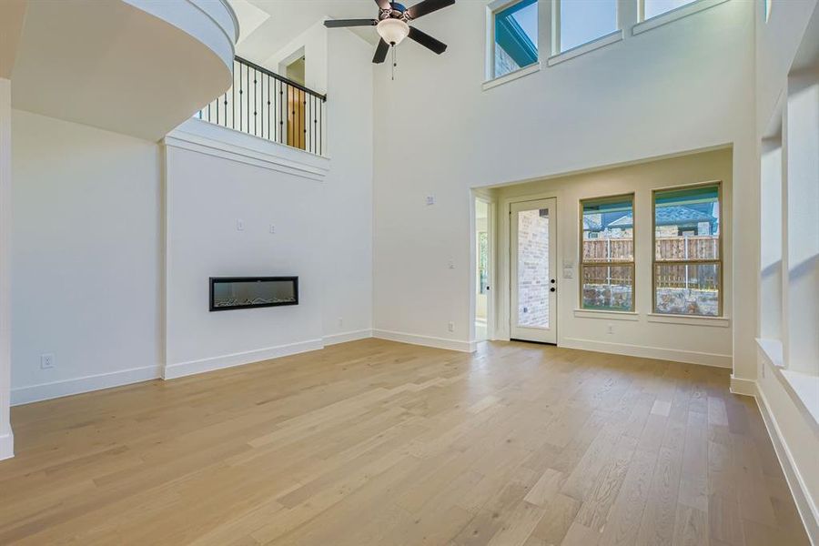 Unfurnished living room featuring a glass covered fireplace, light wood-style floors, ceiling fan, and a high ceiling