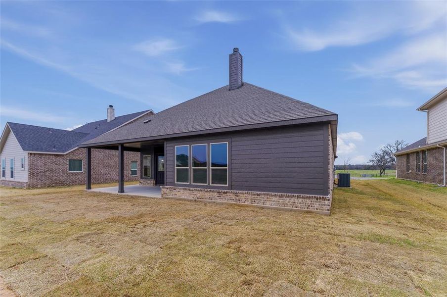 Back of property featuring a chimney, a lawn, roof with shingles, a patio, and brick siding