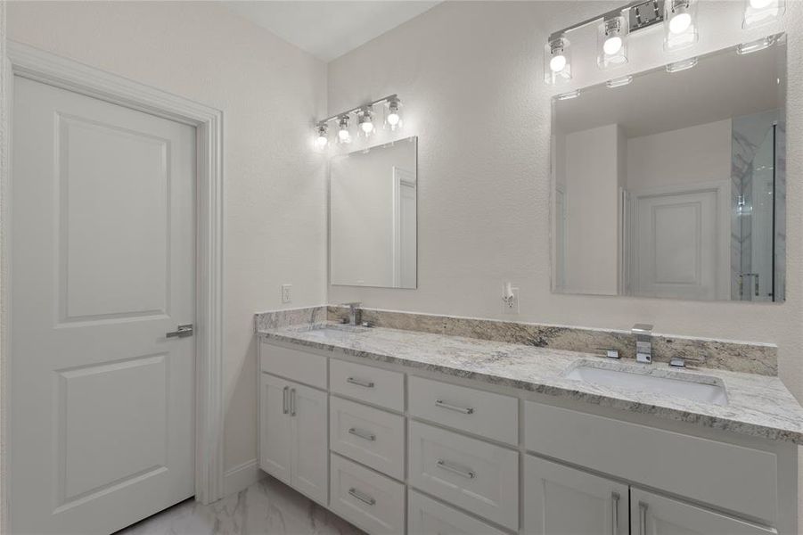 Double vanity featuring white cabinetry, integrated sinks, chrome fixtures, and a light-toned stone countertop Double vanity featuring white cabinetry, integrated sinks, chrome fixtures, and a light-toned stone countertop