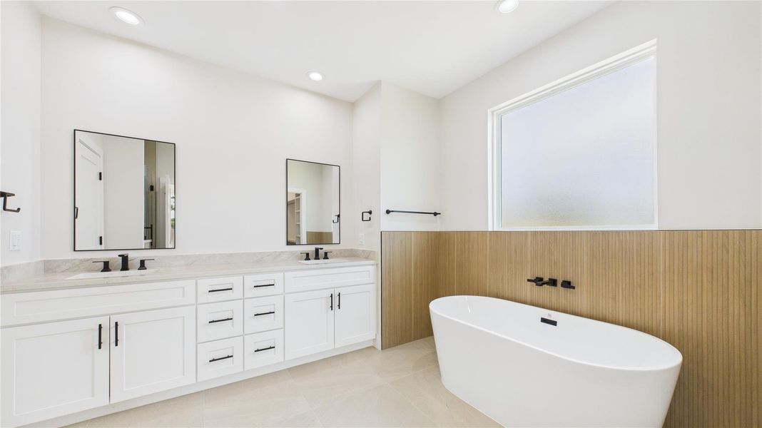 Primary bathroom features a modern design with a double vanity, sleek black fixtures, and ample storage. It includes a freestanding bathtub, large frosted window for privacy, and a clean, minimalist aesthetic. Primary bathroom features a modern design with a double vanity, sleek black fixtures, and ample storage. It includes a freestanding bathtub, large frosted window for privacy, and a clean, minimalist aesthetic.
