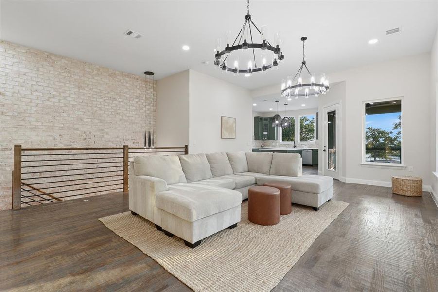 Spacious open-concept room featuring wood-finish flooring, a whitewashed brick accent wall, and contemporary chandeliers Spacious open-concept room featuring wood-finish flooring, a whitewashed brick accent wall, and contemporary chandeliers