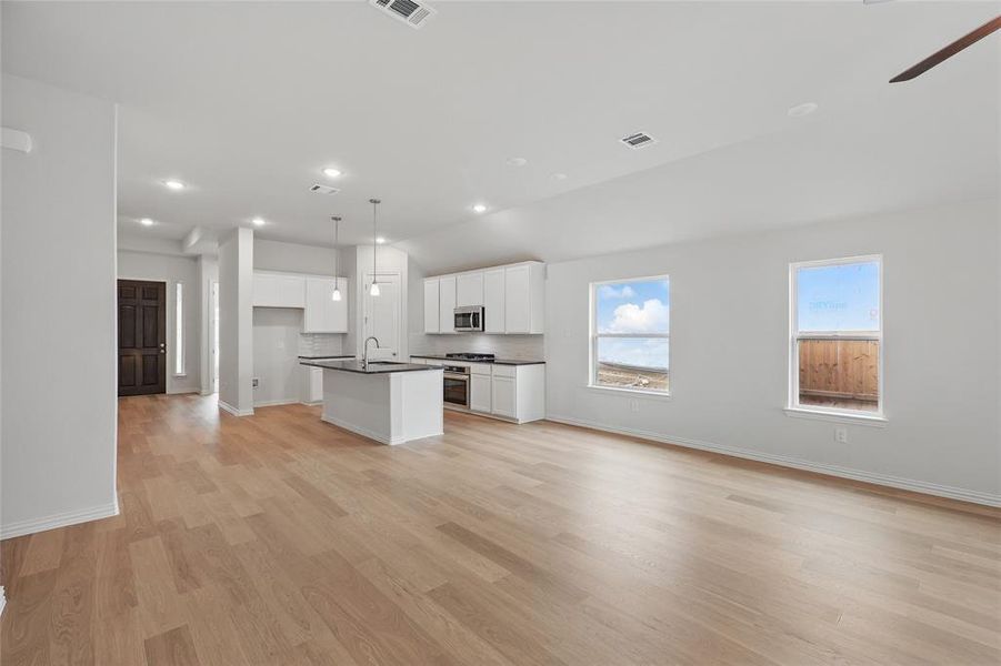 Kitchen featuring a kitchen island with sink, white cabinets, dark countertops, open floor plan, and vaulted ceiling