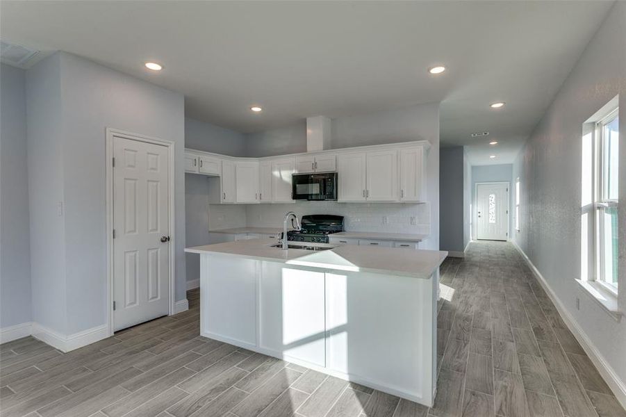 Kitchen with white cabinetry, a kitchen island with sink, black appliances, and light hardwood / wood-style floors