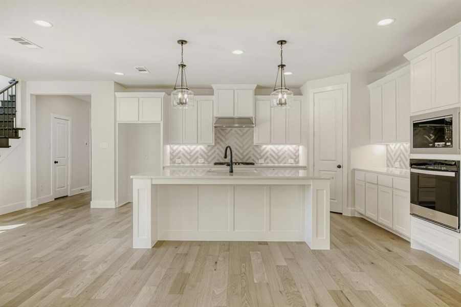 Kitchen with stainless steel appliances, white cabinets, a kitchen island with sink, and decorative light fixtures