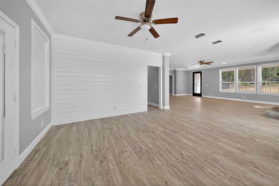 Unfurnished living room featuring crown molding, light wood-style floors, ceiling fan, and wood walls