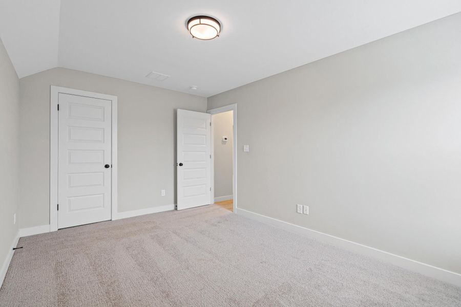 Carpeted room featuring light gray walls, white baseboards, and two white panel doors with black hardware Carpeted room featuring light gray walls, white baseboards, and two white panel doors with black hardware
