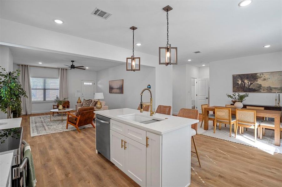 Kitchen with white cabinets, an island with sink, dishwasher, sink, and decorative light fixtures