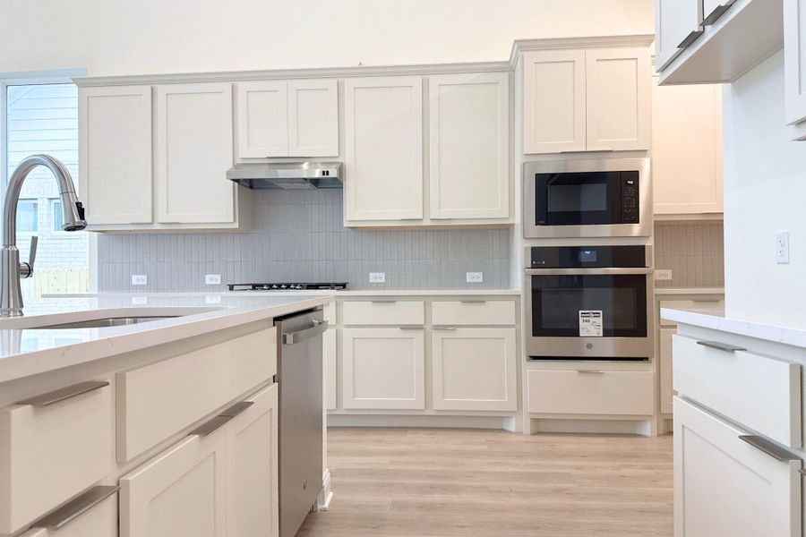 Kitchen with stainless steel appliances, light stone countertops, light wood-type flooring, and backsplash
