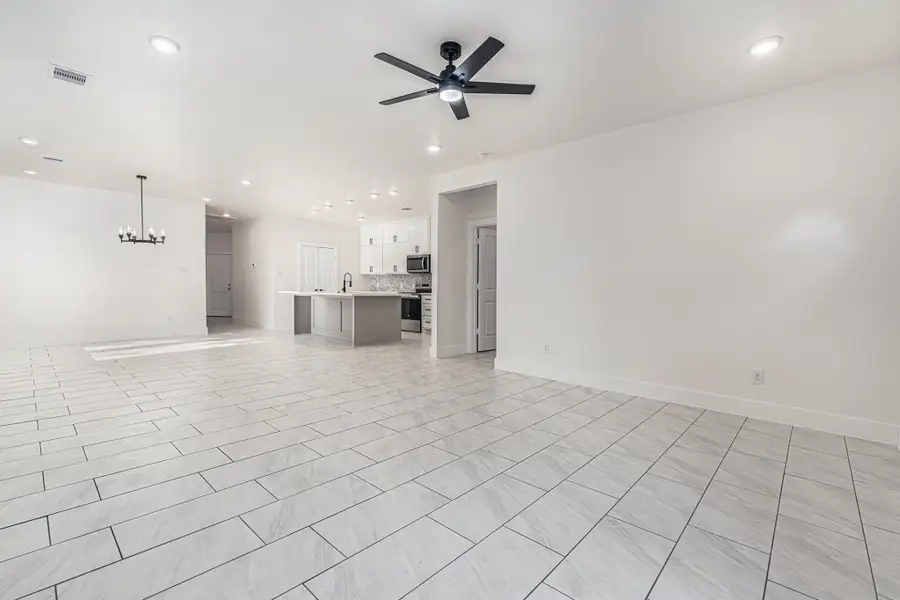 This spacious open-concept living area features modern tile flooring, a ceiling fan, recessed lighting, and a sleek kitchen with an island and stainless steel appliances. Perfect for entertaining and family living.