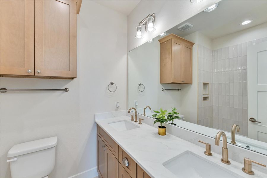 Secondary bathroom featuring a dual-sink vanity and tiled walk-in shower.