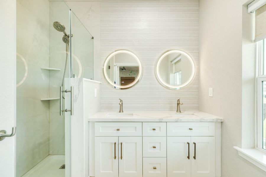 Spa-inspired primary bath features a dual-sink quartz vanity, illuminated mirrors, and a spacious walk-in glass shower with elegant tile finishes.