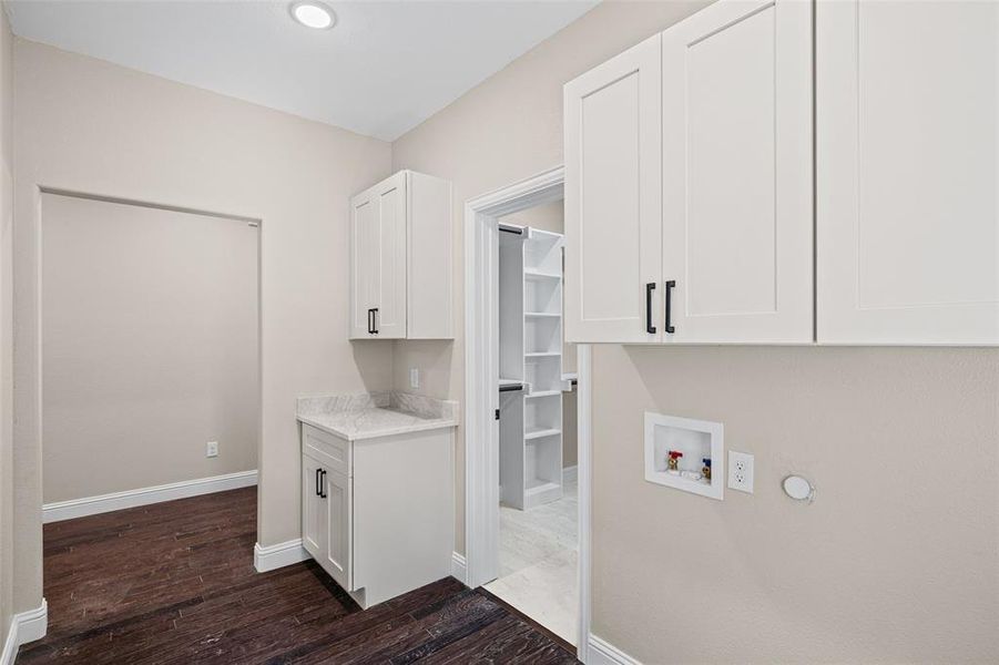 Bright utility space featuring white shaker-style cabinetry, a built-in countertop, and dark wood-finish flooring