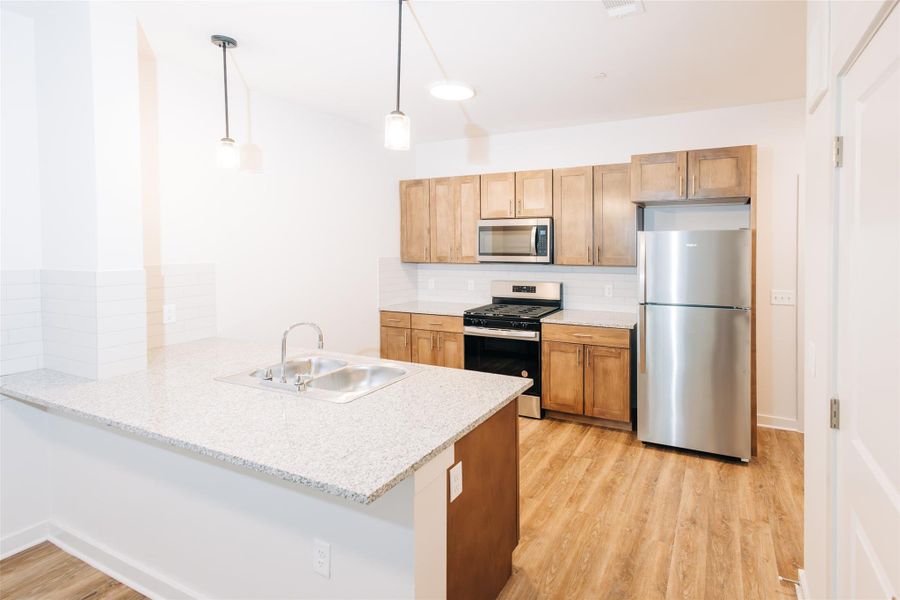 Kitchen featuring appliances with stainless steel finishes, a peninsula, decorative backsplash, light wood-style floors, and hanging light fixtures