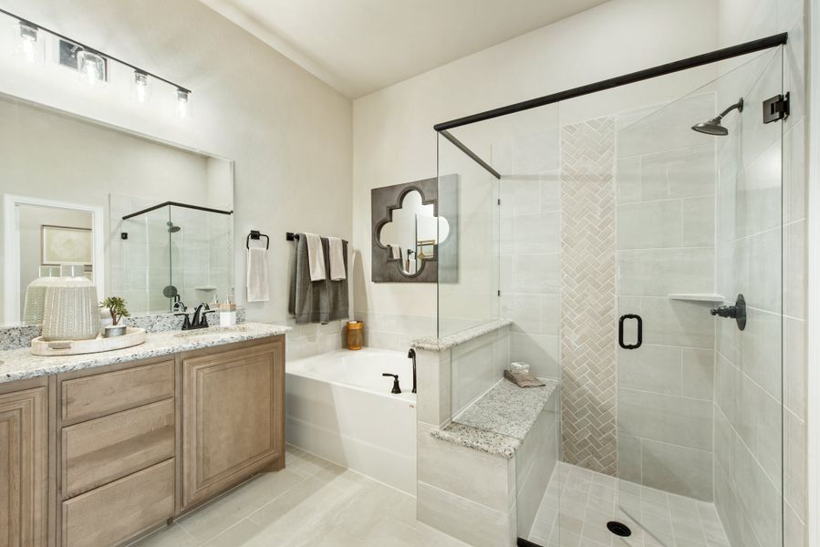 Bathroom with wood vanity, granite countertop, soaking tub, and glass-enclosed walk-in shower with herringbone tile