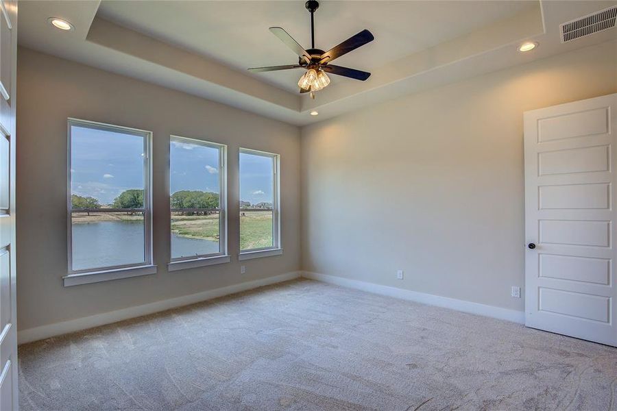 Unfurnished room with carpet, a raised ceiling, a water view, and ceiling fan