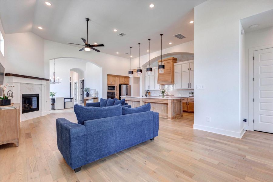 This spacious living room features high ceilings, recessed lighting, and a ceiling fan. It includes a cozy fireplace, large windows for natural light, and stylish blue seating. The open layout leads to a dining area with a modern chandelier, enhancing the home's airy feel. This spacious living room features high ceilings, recessed lighting, and a ceiling fan. It includes a cozy fireplace, large windows for natural light, and stylish blue seating. The open layout leads to a dining area with a modern chandelier, enhancing the home's airy feel.