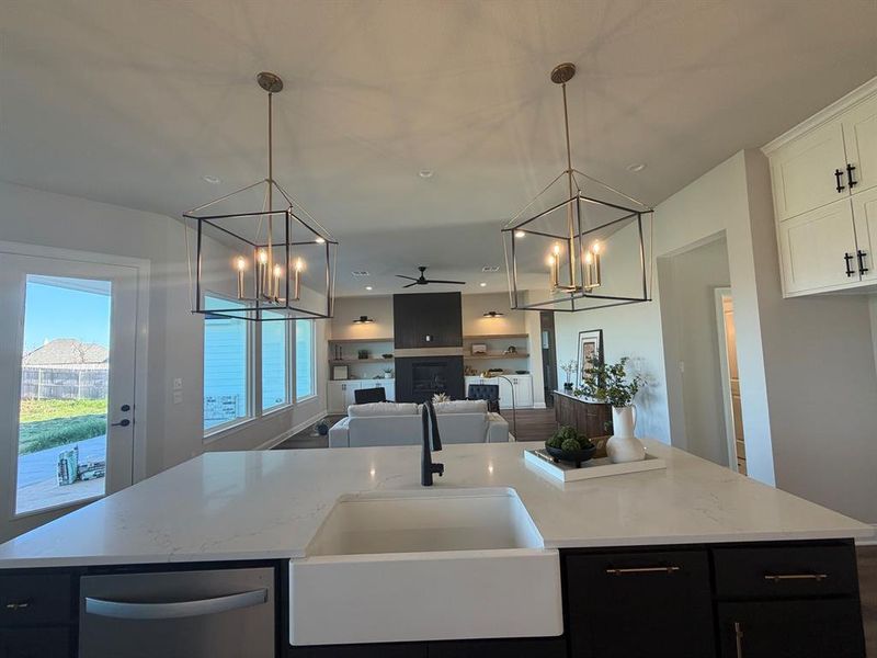 Kitchen featuring a chandelier, a ceiling fan, a kitchen island with sink, dark cabinets, and open floor plan