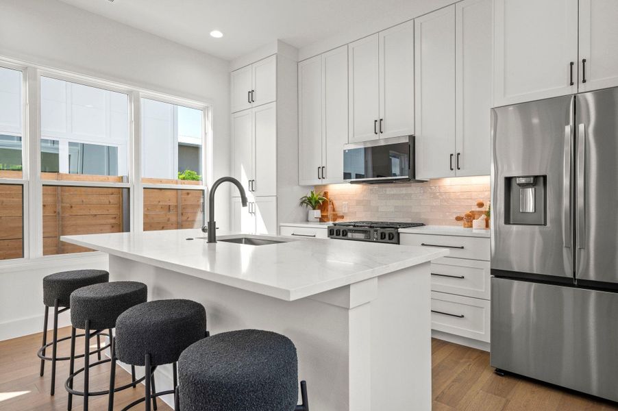 Kitchen with appliances with stainless steel finishes, tasteful backsplash, white cabinets, light stone countertops, and a kitchen island with sink Kitchen with appliances with stainless steel finishes, tasteful backsplash, white cabinets, light stone countertops, and a kitchen island with sink