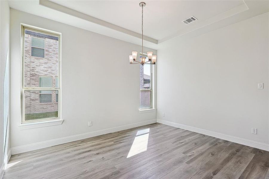 Spare room with a raised ceiling, an inviting chandelier, and wood-type flooring