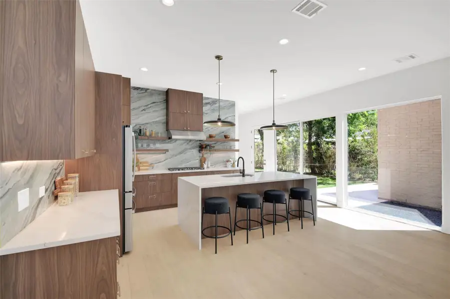 Kitchen featuring open shelves, modern cabinets, a breakfast bar, light quartz counters, and a kitchen island with sink