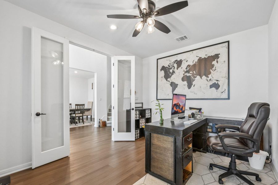 A vibrant home office features ample desk space and stylish glass-paned doors.