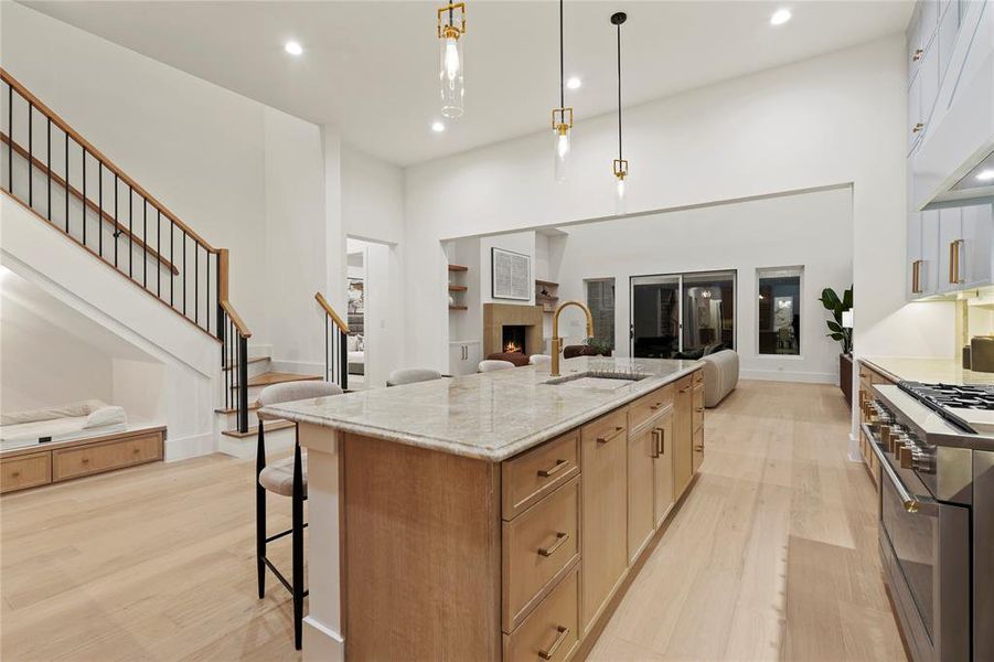 Kitchen featuring a kitchen breakfast bar, open floor plan, light wood-style floors, a center island with sink, and a lit fireplace