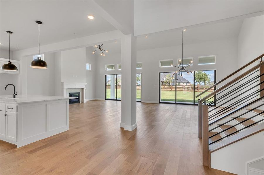 Unfurnished living room with sink, light hardwood / wood-style flooring, a chandelier, and a high ceiling