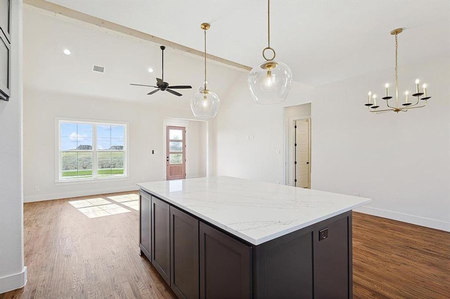 Kitchen featuring hanging light fixtures, dark hardwood / wood-style flooring, ceiling fan with notable chandelier, dark brown cabinetry, and light stone counters