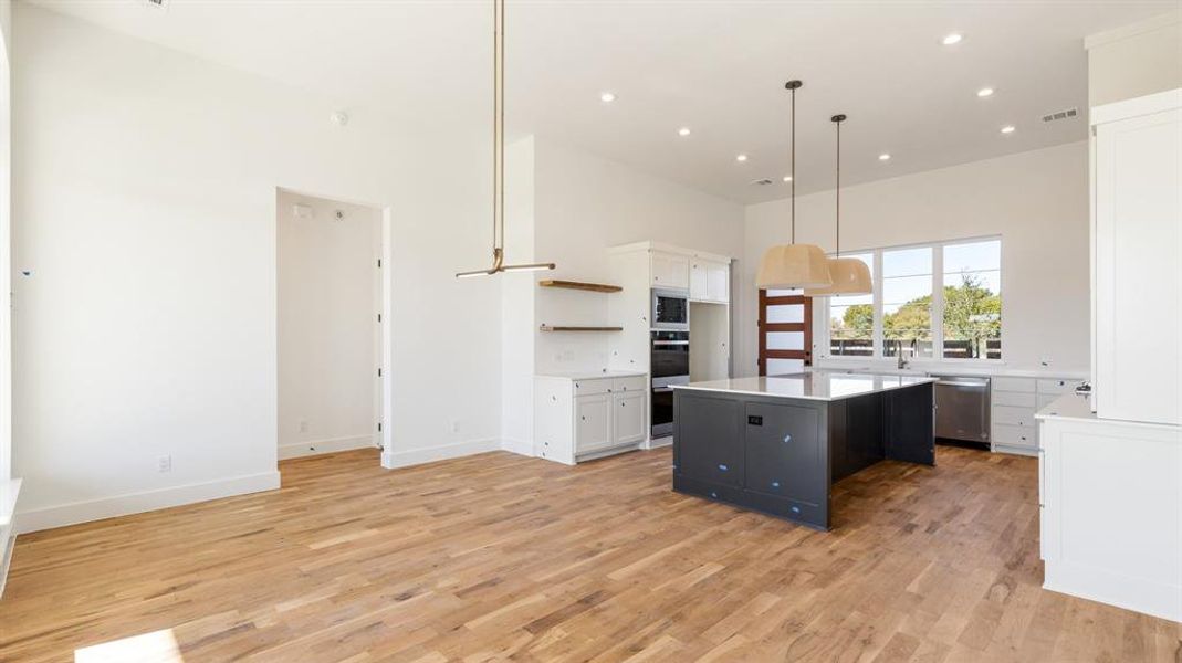 Kitchen with decorative light fixtures, a kitchen island, white cabinetry, and appliances with stainless steel finishes