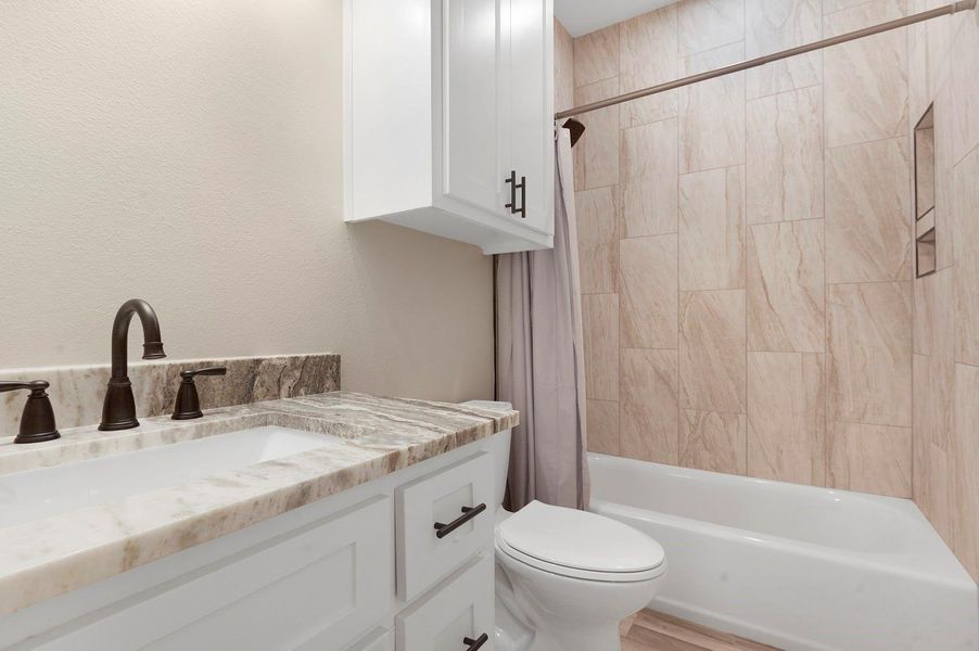This bathroom features a sleek design with a marble countertop, dark fixtures, white cabinetry, and a tiled shower-tub combo, offering a modern and clean look. This bathroom features a sleek design with a marble countertop, dark fixtures, white cabinetry, and a tiled shower-tub combo, offering a modern and clean look.