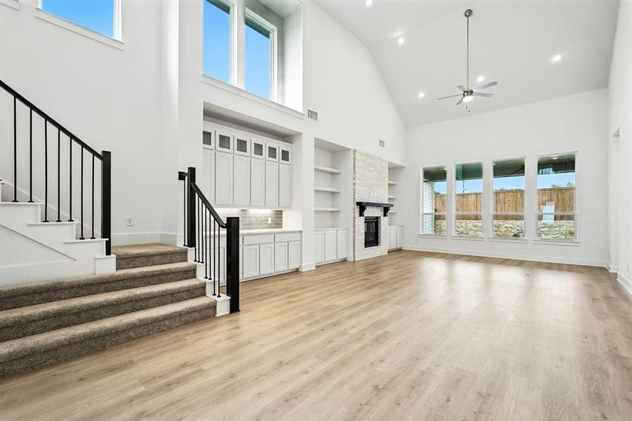 Unfurnished living room featuring high vaulted ceiling, a fireplace, stairs, a ceiling fan, and light wood-style floors Unfurnished living room featuring high vaulted ceiling, a fireplace, stairs, a ceiling fan, and light wood-style floors