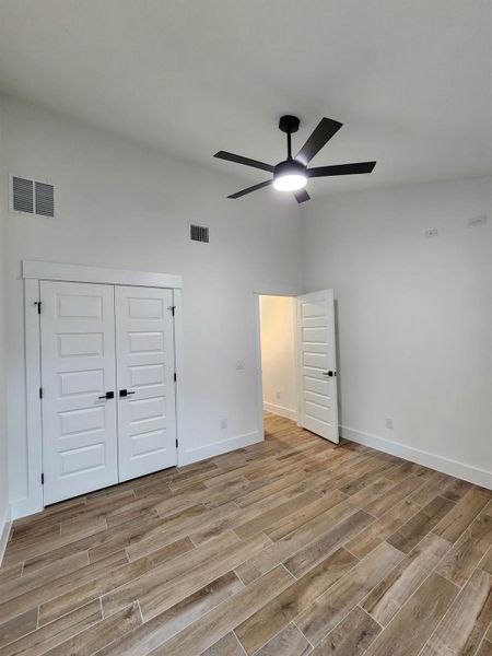 Unfurnished bedroom featuring wood tiled floors, a ceiling fan, a towering ceiling, and a closet