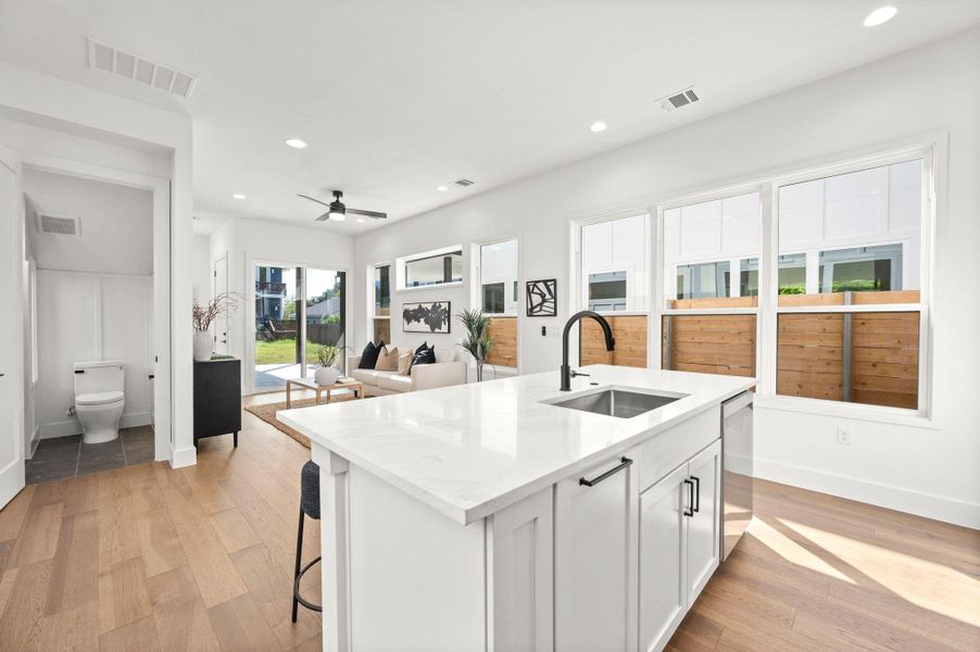 Kitchen with white cabinetry, light stone countertops, a kitchen island with sink, ceiling fan, and light wood-style flooring