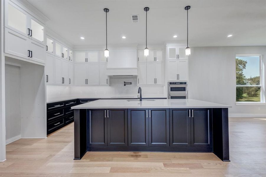 Contemporary kitchen featuring a large central island with dark cabinetry, complemented by white upper and dark lower perimeter cabinetry