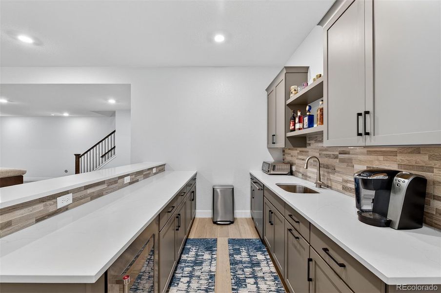 Basement Wet Bar (Close View) – Modern bar area with sleek gray cabinetry, under-counter appliances, and open shelving for glassware and display.