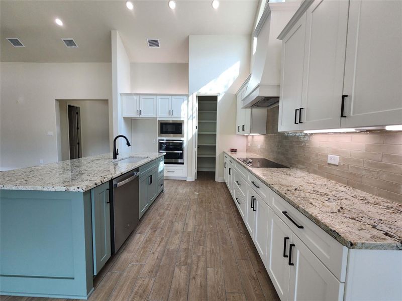 Dual tone kitchen with two tone cabinetry, light stone counters, an island with sink, dark wood-type flooring, and stainless steel appliances