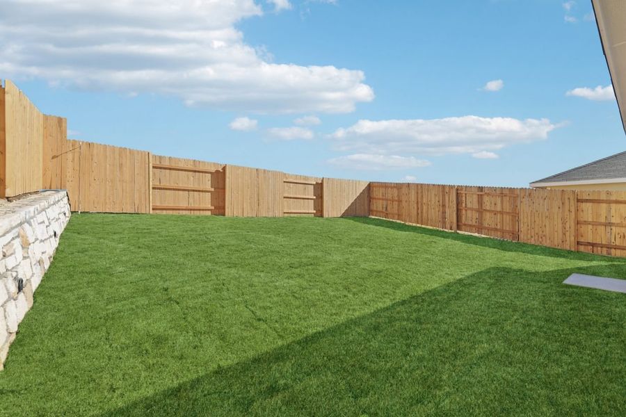 Image of a green grass back yard with a wooden fence and a cloudy blue sky