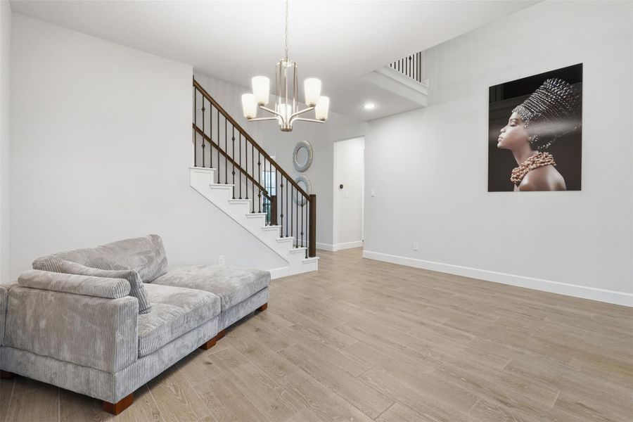 This photo shows a modern living space with light wood flooring, a cozy gray sectional sofa, and a stylish chandelier. A staircase with dark wooden railing leads to the upper level, and a contemporary art piece adorns the wall, adding a touch of elegance. This photo shows a modern living space with light wood flooring, a cozy gray sectional sofa, and a stylish chandelier. A staircase with dark wooden railing leads to the upper level, and a contemporary art piece adorns the wall, adding a touch of elegance.