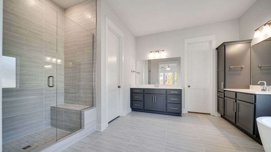 Large tiled bathroom with multiple vanities, glass shower enclosure, and freestanding tub
