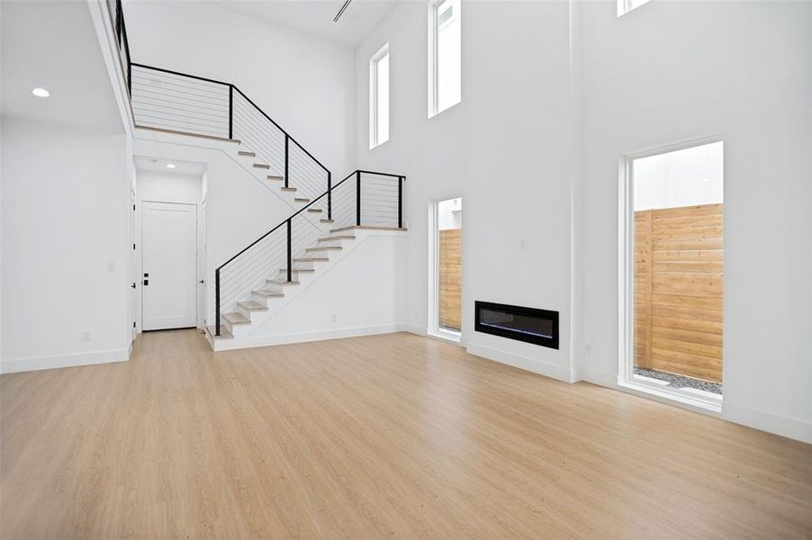 Open-concept living area featuring high ceilings, light wood-finish flooring, and a contemporary linear fireplace