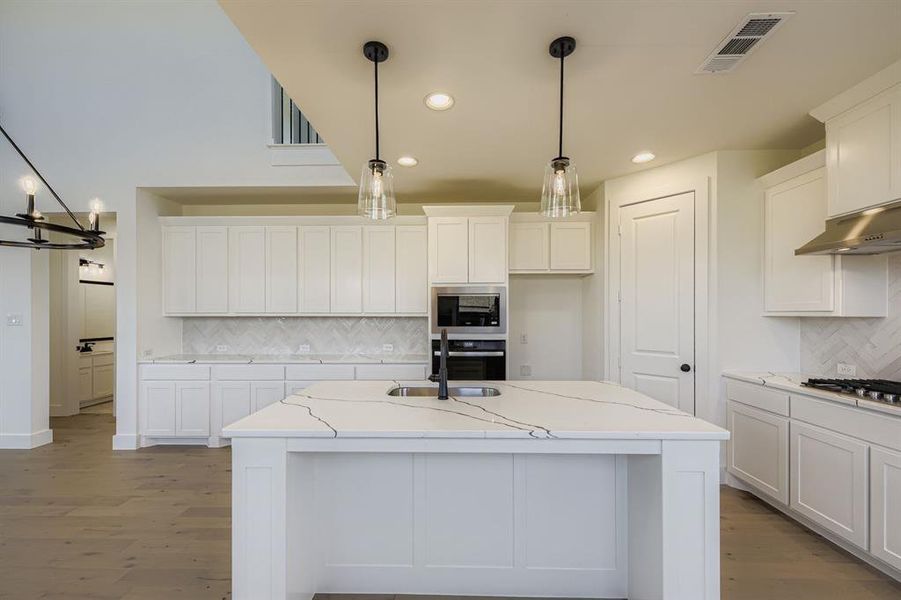 Kitchen featuring tasteful backsplash, decorative light fixtures, dark wood-style floors, white cabinets, and light stone countertops